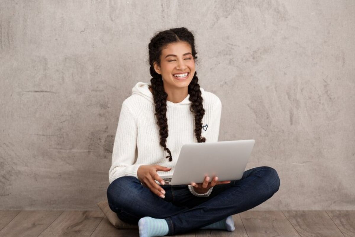 Uma menina sentada no chão com o notebook no colo se inscreve nos cursos ETEC 2025