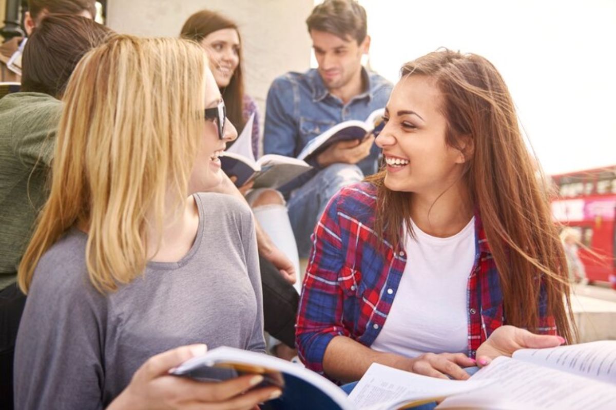 Duas alunas da ETEC Campinas 2025 na sala de aula compartilham um livro. Ao fundo é possível ver outros três colegas 