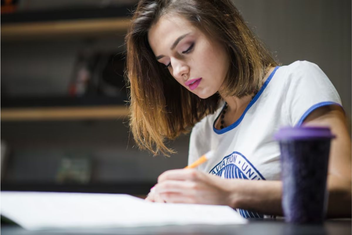 Uma menina dentro de sua casa escreve no caderno. Ela estuda para garantir uma vaga na Etec