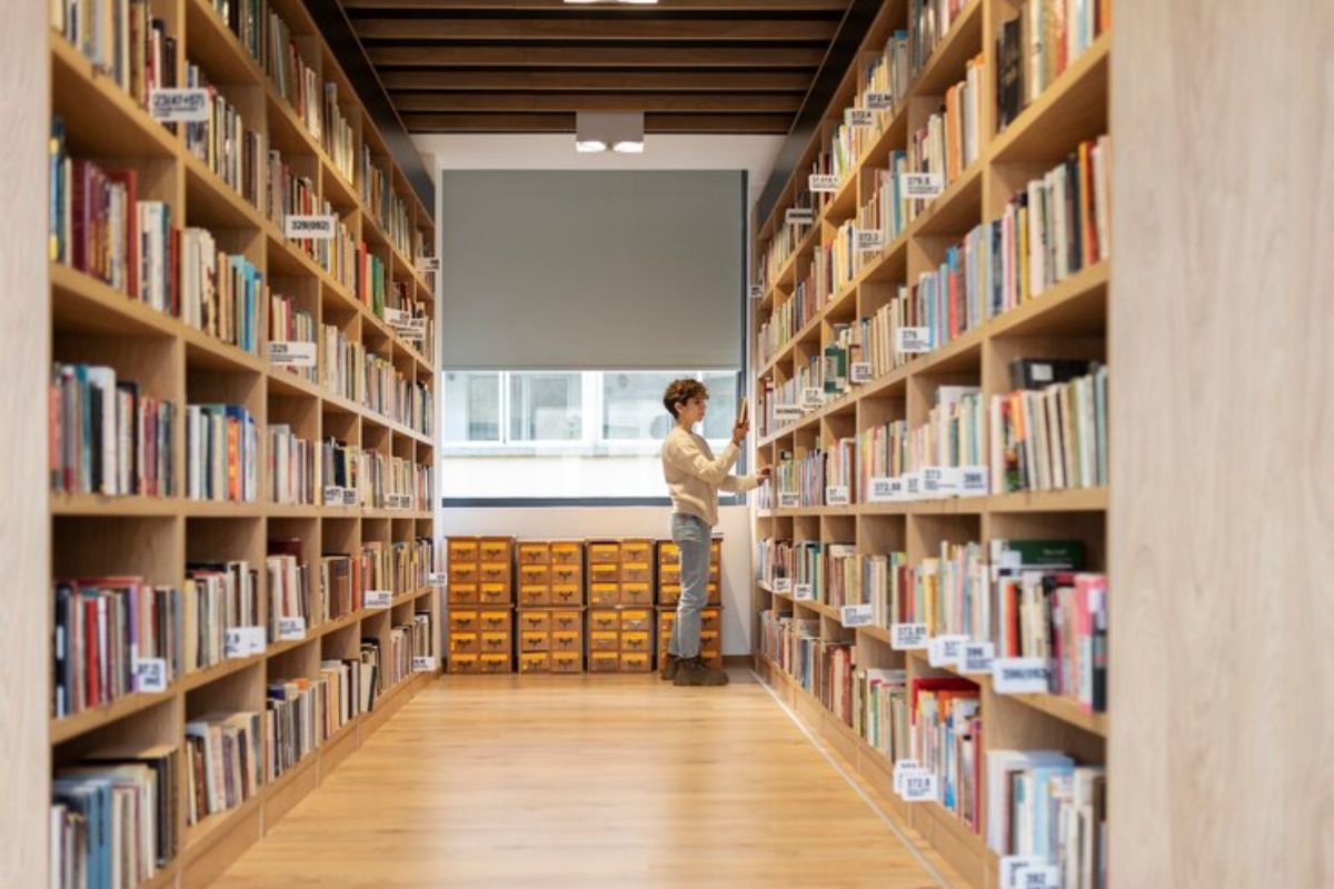 Uma pessoa está no corredor da biblioteca procurando um livro na estante