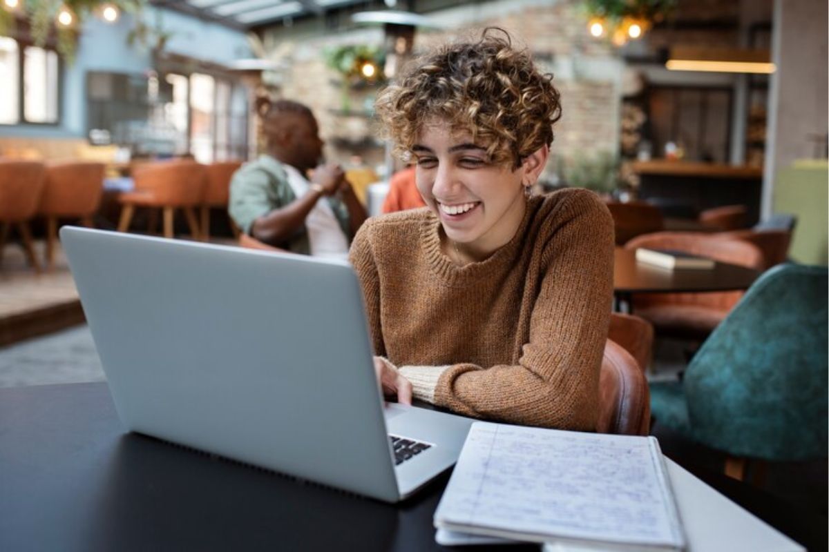 Uma estudante na mesa do refeitório usa seu notebook para acessar a Área do Candidato ETEC 2025