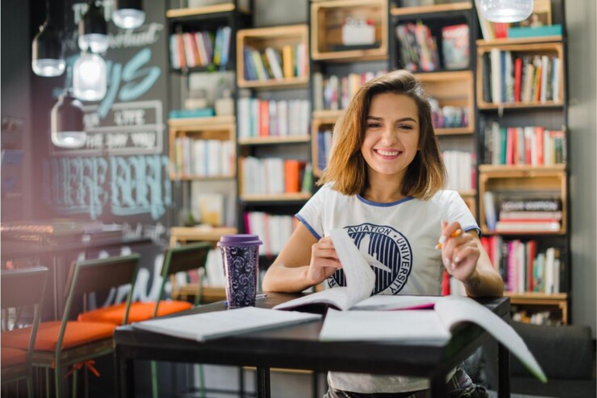 Uma estudante na biblioteca está com um livro aberto na mesa estudando as questões de matemática ETEC 2025