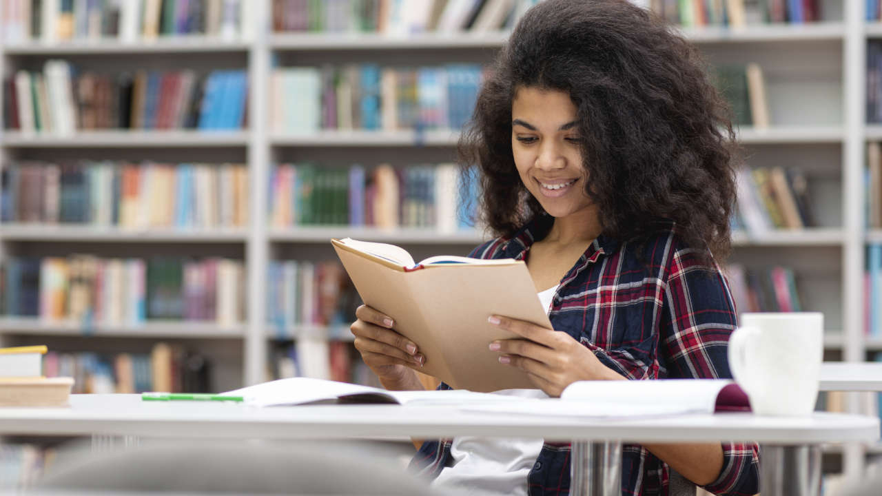 Estudante negra lendo livro em biblioteca