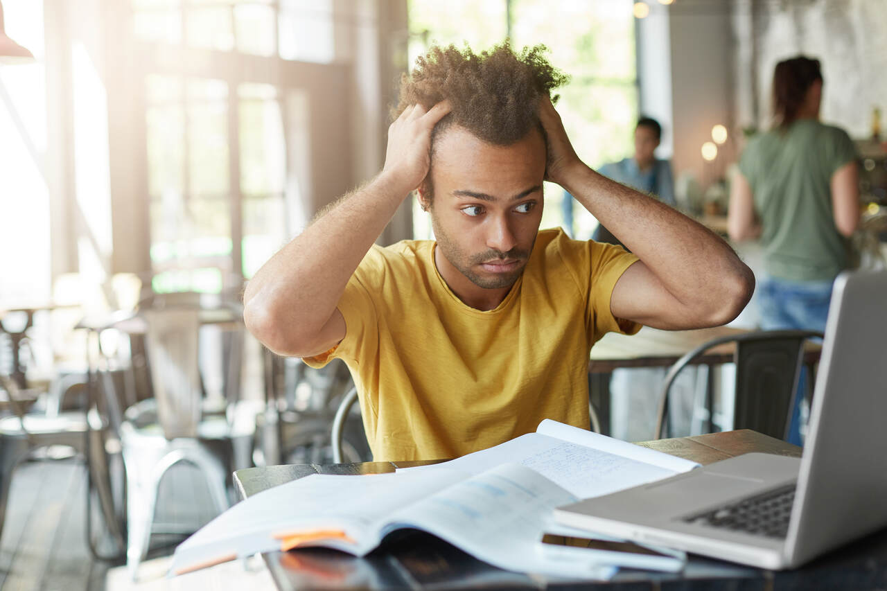 Jovem demonstra estresse enquanto estuda sentado diante o notebook e livros 