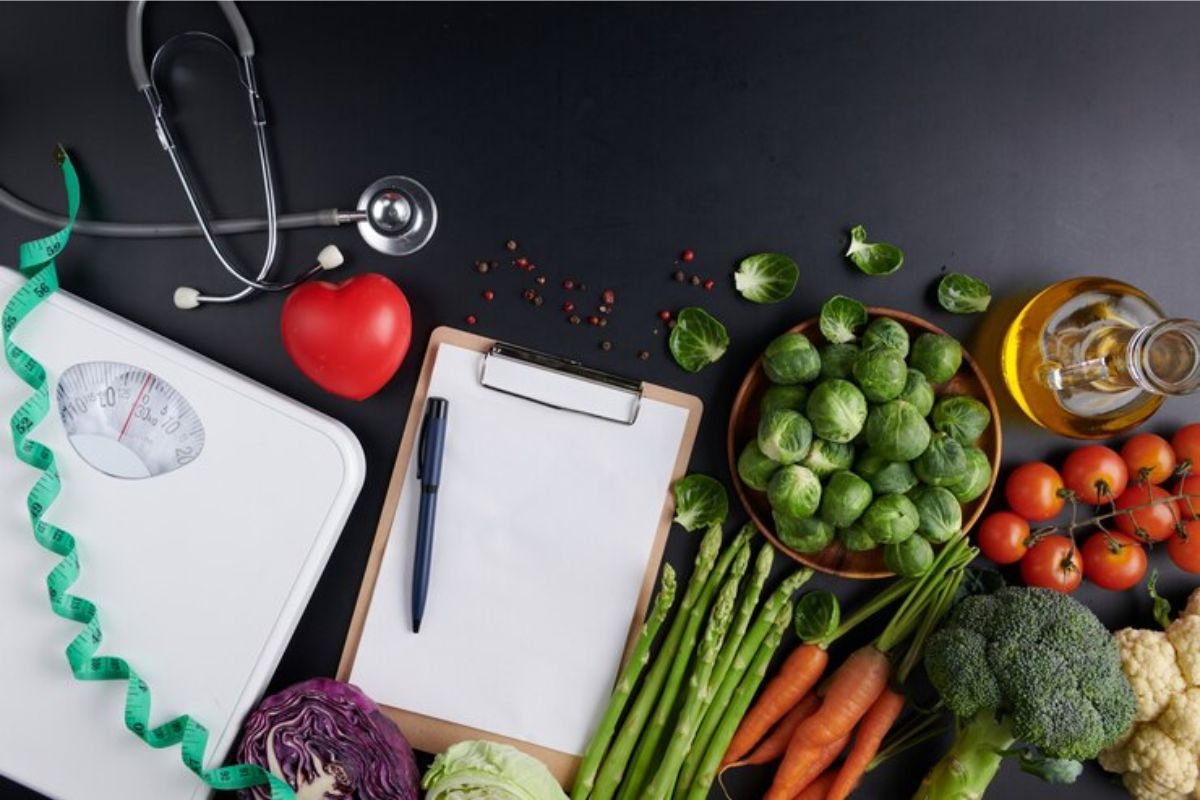 Uma série de alimentos saudáveis em cima da mesa e uma prancheta ao lado de uma balança