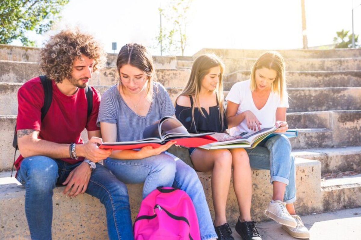 Um grupo de quatro estudantes juntos no pátio da escola, eles estudam juntos